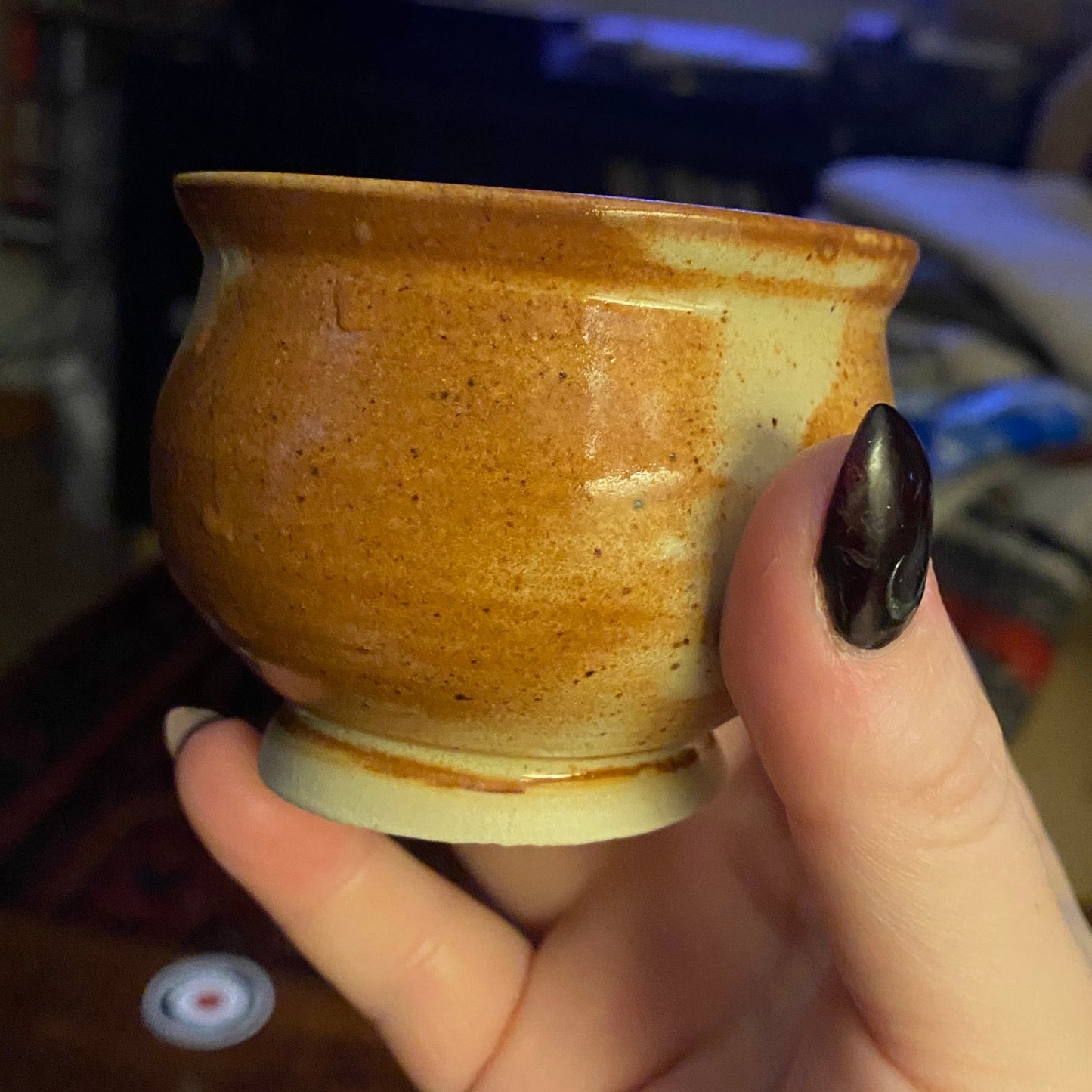 Hand holding a small ceramic cup with a blurred background